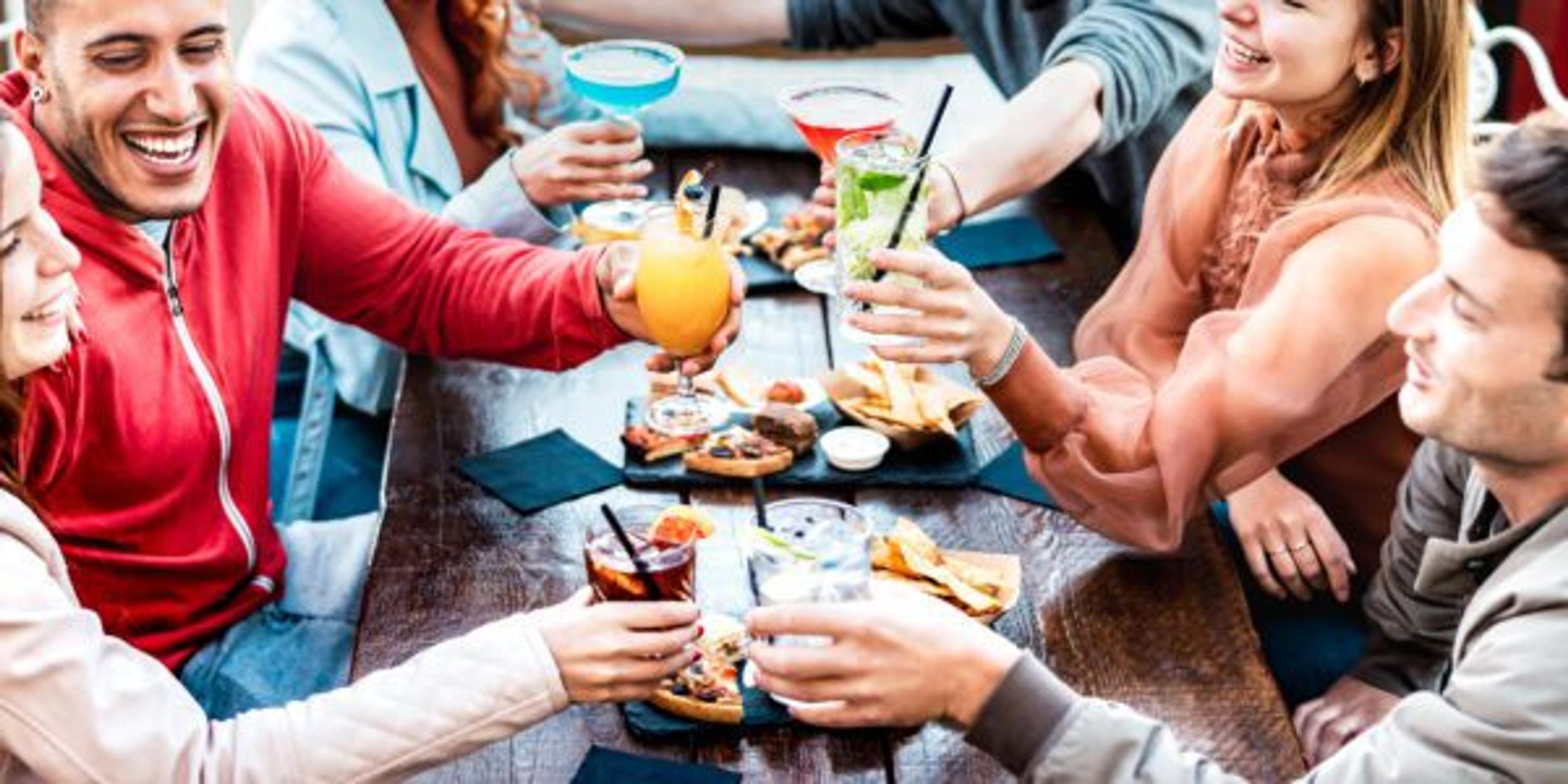 Young adults toast to a good meal while eating outdoors at a restaurant and drinking mocktails.