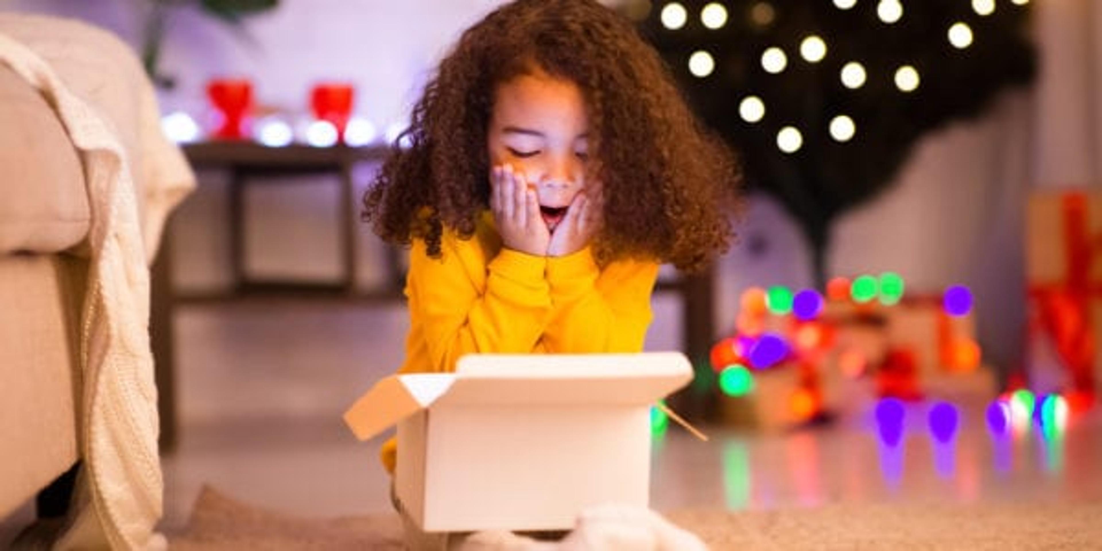 Desired present. Amazed little afro girl opening Christmas gift near xmas tree, free space