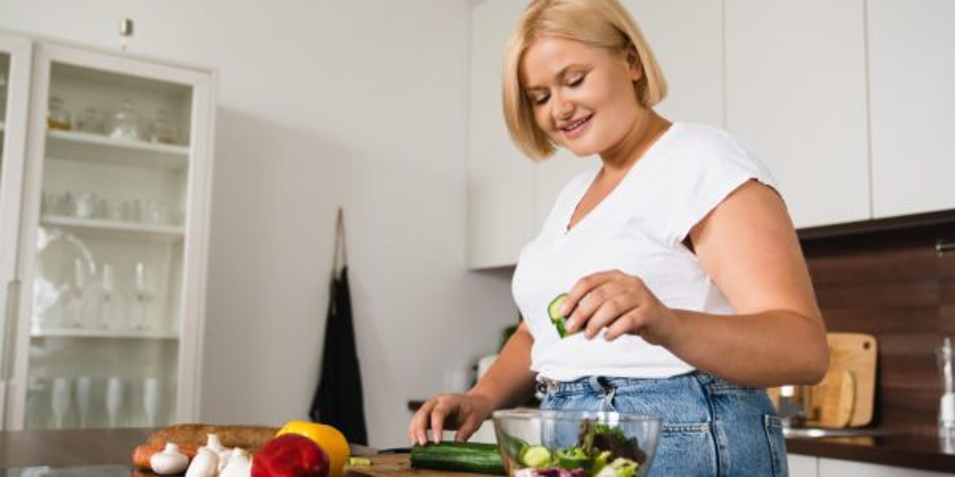 Young caucasian plump plus size woman cooking making salad, healthy food, dieting, counting calories, preparing dinner lunch at home kitchen